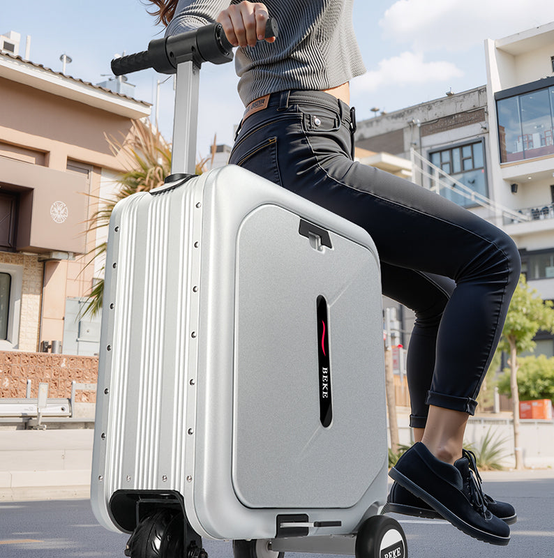 Person sitting on a silver electric suitcase with wheels in an urban setting